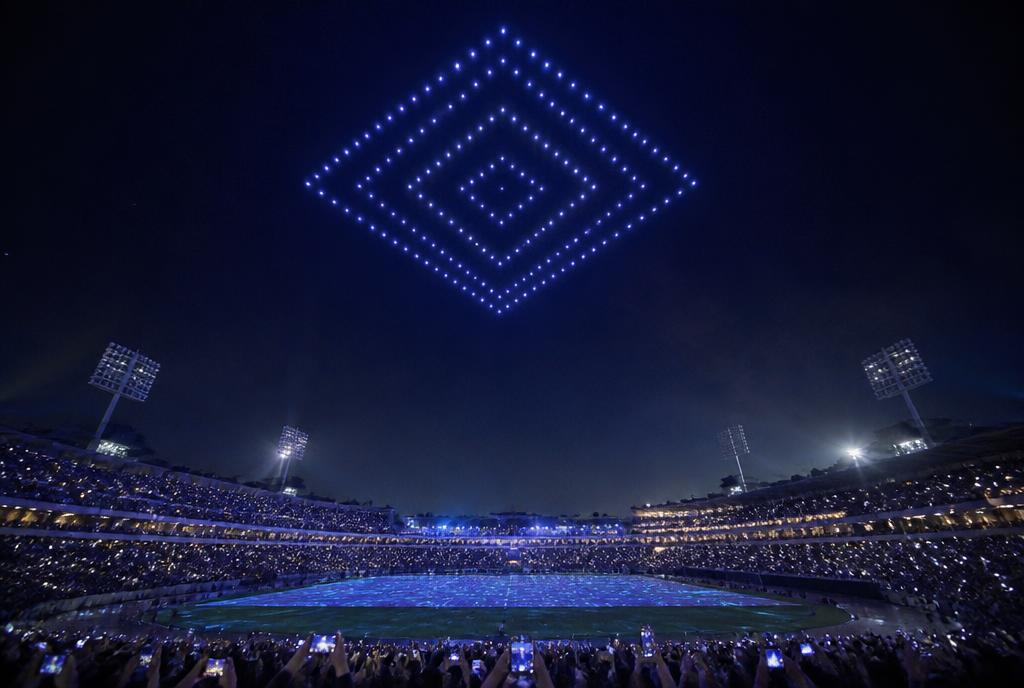 Drone light show forming a glowing shape above a floodlit stadium at night